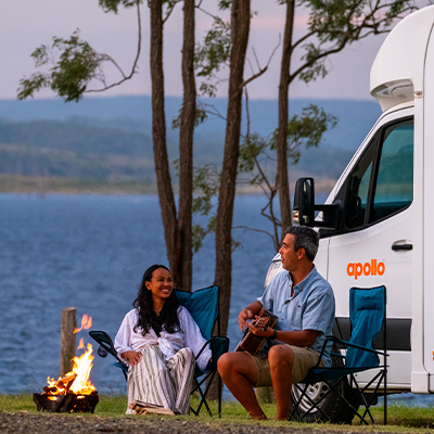 a couple sit by a fire in the Somerset region in Queensland, in front of their Apollo motorhome